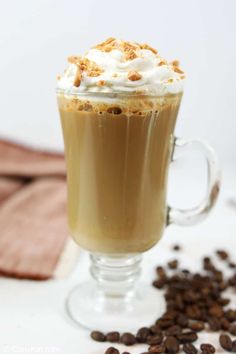 there is a cup of coffee with whipped cream on top and coffee beans around it