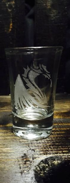 a glass sitting on top of a wooden table next to a black object in the background