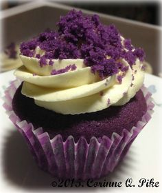 a cupcake with white frosting and purple sprinkles sitting on a plate