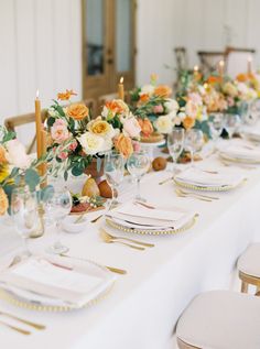 the table is set with white and gold plates, silverware, flowers and candles