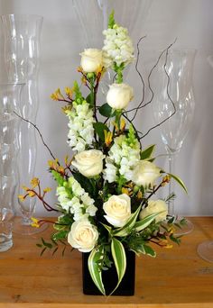 a vase filled with white flowers sitting on top of a table next to wine glasses