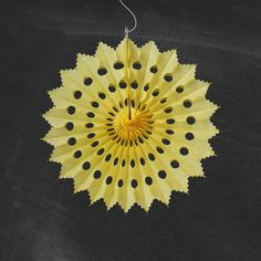 a yellow paper fan hanging from a string on a black surface with holes in it