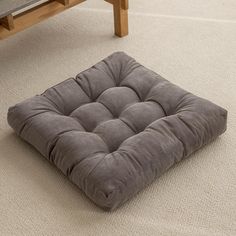 a square dog bed is on the floor in front of a coffee table and bench