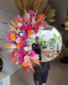 a woman taking a selfie in front of a mirror with colorful flowers on it