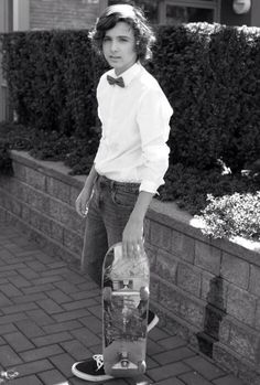 a young boy is holding a skateboard in his hand and wearing a bow tie