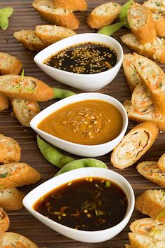 several small bowls filled with dipping sauce next to bread rolls