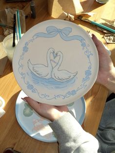 a person holding up a plate with two swans painted on the front and back of it