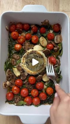 a person holding a fork over a dish with tomatoes and mushrooms