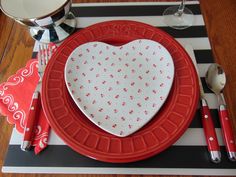 a red and white heart shaped plate on a place mat with utensils next to it