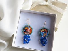 Sicilian style earrings made of: - Lava rock tiles decorated on a side with Sicilian Ceramic; - Faceted stones (6 mm), blue color; - Brass open hooks. Tile Diameter: 25 mm Lenght : 5,5 cm / 2,17 inches * SHIPPING * Your order will be shipped within 1-3 business days from your purchase. You can choose between 2 shipping methods: STANDARD SHIPPING (without tracking) or REGISTERED MAIL (with tracking). Each chapeau atelier jewel is shipped in a gift box. Thank you for your visit. Round Beaded Earrings With Natural Stones As Gift, Round Natural Stones Beaded Earrings As Gift, Handmade Blue Cluster Earrings For Gift, Blue Natural Stone Earrings As Gift, Blue Cluster Drop Earrings As Gift, Blue Drop Cluster Earrings For Gift, Rock Tile, Sicilian Style, Tile Earrings