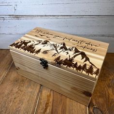 a wooden box with mountains and trees engraved on the lid, sitting on a wood floor