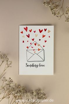 a greeting card with hearts coming out of an envelope on a pink background next to flowers