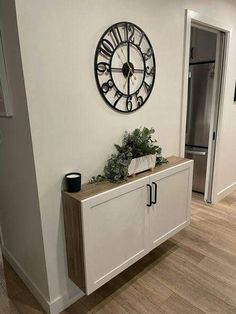 a clock mounted to the side of a wall next to a cabinet with plants on it