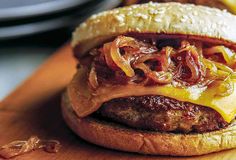 a cheeseburger with onions and meat on a wooden cutting board, ready to be eaten