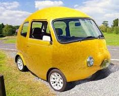 a small yellow car is parked on the side of the road in front of a grassy field