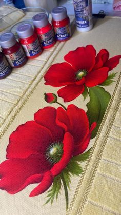 some red flowers are sitting on a table next to thread markers and paint bottles in front of them