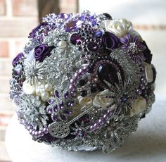 the bridal bouquet is adorned with purple and white flowers, brooches and pearls