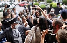 a crowd of people taking pictures with their cell phones and wearing face masks while standing in the street