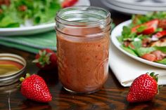 there is a mason jar with some strawberries on the table next to it and salad in the background