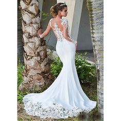 a woman in a white wedding dress standing next to a palm tree and looking off into the distance