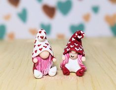 two small figurines sitting next to each other on a wooden surface with hearts in the background