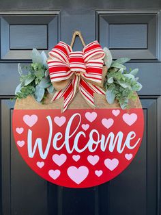 a welcome sign hanging on a door with hearts and greenery in the shape of a heart