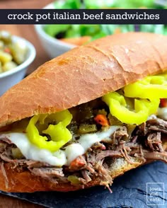 a close up of a sandwich with meat and vegetables in it on a plate next to a bowl of salad