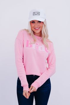 Our Bride Sweatshirt is a must have for a new bride or bride-to-be, perfect to pair with your fav denim for a cute OOTD. Features a pink jersey fabric, a round neck, a full length sleeve with banded cuff, a ribbed banded hem, and "Bride" across the front in multi-color pink font with the a heart as the dot on the I. Fit: Comfy fit, model is wearing a small. Approximate Measurements: Small- Bust: 38" Length: 26" Medium- Bust: 40" Length: 26.5" Large- Bust: 42" Length: 26" XL - Bust: 44" Length: 2