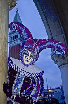 a purple and white costumed person in front of a clock tower