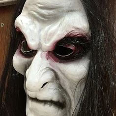 a close up of a person wearing a white mask with black hair and red eyes