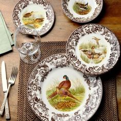 three plates with birds painted on them sitting on a place mat next to silverware