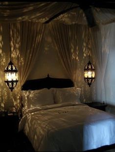 a bed sitting under a canopy in a bedroom next to two lamps on either side of the bed