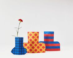 three different colored vases with a single flower in them and one is made out of paper