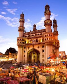 an outdoor market with lots of people and tents in front of it at dusk time