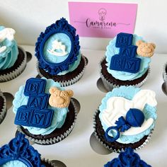 there are many cupcakes that have blue icing on them and decorations in the shape of baby items