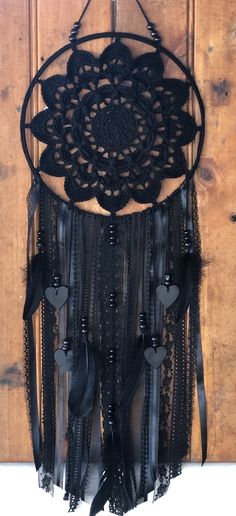 a black crochet doily hanging on a wooden door with feathers and ribbons