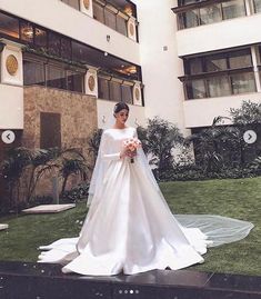 a woman in a white wedding dress standing on the grass near a large hotel building