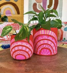 two pink vases with plants in them sitting on a table next to colorful pillows