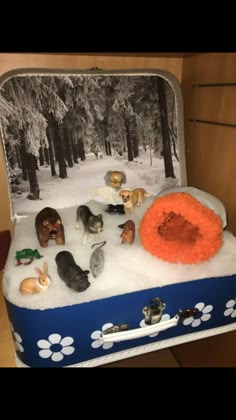 an open suitcase filled with toy animals and snow covered ground in front of a forest