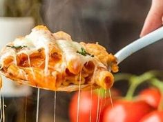 a person is holding a spoon full of pasta and sauce with tomatoes in the background