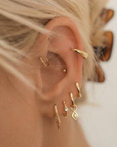 a close up of a person wearing gold ear cuffs and piercings on their ears