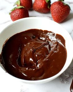 a white bowl filled with chocolate and strawberries on top of a marble countertop