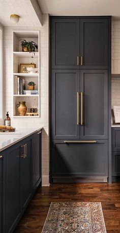 a kitchen with dark gray cabinets and gold pulls on the doors, along with a rug