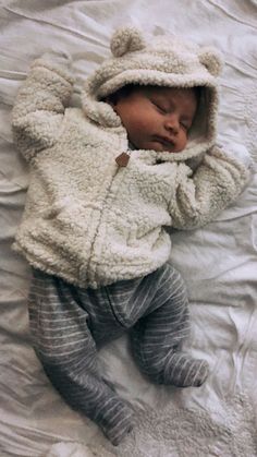 a baby sleeping on top of a bed wearing a teddy bear jacket