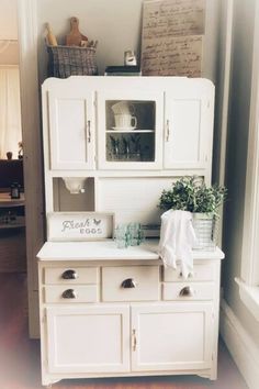 an old fashioned white kitchen cabinet with drawers and cupboards on the top, next to a potted plant