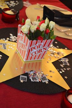 a popcorn box centerpiece with roses in it sitting on a star shaped table cloth