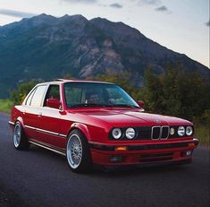 the red car is parked on the side of the road in front of some mountains