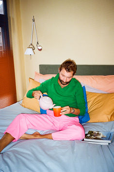 a man sitting on top of a bed next to a woman holding a tea pot