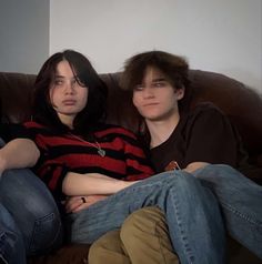 two people sitting on a couch with their arms around each other and one person looking at the camera