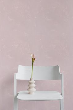 a white chair with a pink wall and a flower in it's vase on the seat